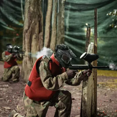 Aim. Shoot. Conquer. A player takes cover and fires during an intense paintball match in our wooded arena.