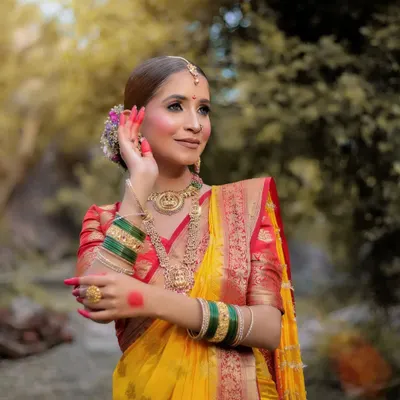 A beautiful outdoor portrait of a model in a traditional yellow Maharashtrian saree, her pose graceful and elegant.