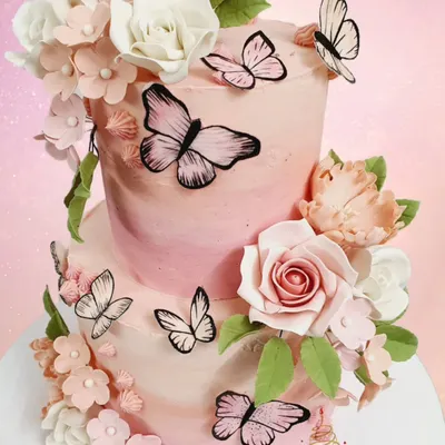 A close-up of a two-tier buttercream cake, showcasing the delicate wafer-paper butterflies and handcrafted sugar flowers in soft shades of pink.