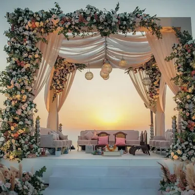 A romantic sunset mandap on a beach, with lush floral pillars and soft, flowing drapes. This setup is perfect for an intimate and picturesque destination wedding.