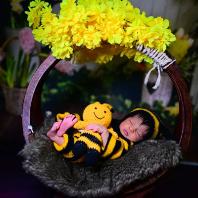 An adorable newborn photoshoot featuring our bumblebee costume. The baby is sleeping peacefully in a basket, complete with a matching toy and yellow flowers.