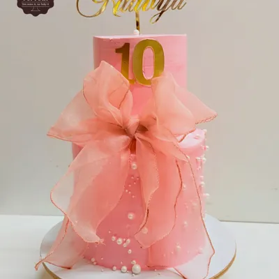A pretty pink two-tier cake for a 10th birthday, decorated with a large, delicate organza bow. This design is simple, elegant, and very chic.
