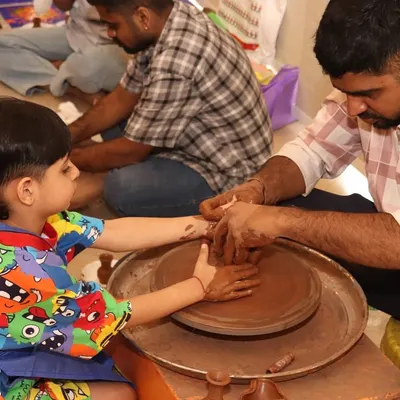 An instructor guides a child's hands as they learn to center clay on the pottery wheel. It's a wonderful sensory activity that teaches physics in a creative way.