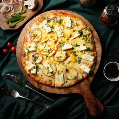 A top-down view of a delicious paneer pizza, fresh and ready to eat. We styled it with fresh ingredients on the side to emphasize its quality.