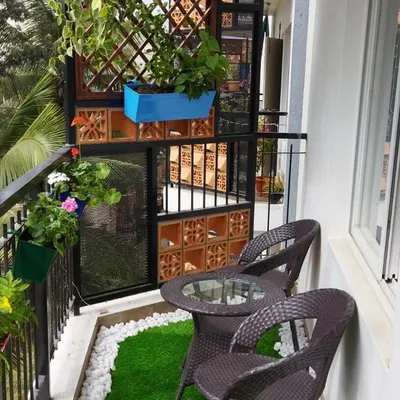 We designed this cozy balcony seating nook, complete with a small table and chairs. The space is decorated with railing planters, a wooden trellis with a climbing plant, and artificial grass with a white pebble border.