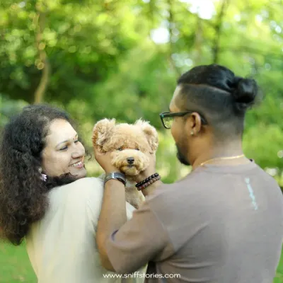 A family portrait in a lush Malaysian park, where a couple lovingly holds their poodle, showcasing the central role pets play in our lives.