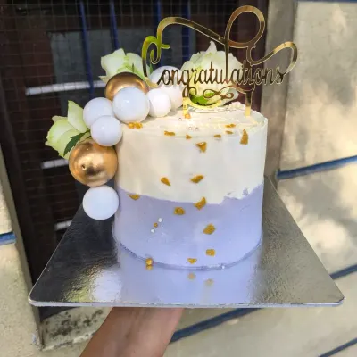This lilac and gold cake is a dream for any elegant celebration. The combination of soft lavender buttercream, shimmering gold leaf, decorative spheres, and fresh white flowers creates a sophisticated and modern look.