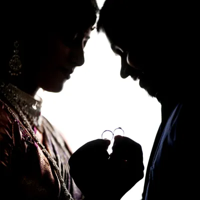 A creative silhouette shot focusing on the couple's hands as they hold their engagement rings.
