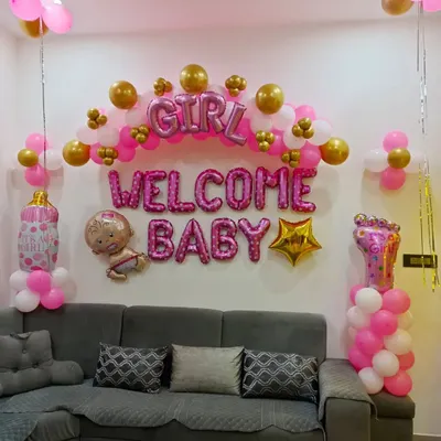 A classic "Welcome Baby" decoration for a home living room. This setup uses pink and gold balloons, foil letters, and baby-themed props to create a festive atmosphere for welcoming a baby girl.