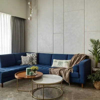 The centerpiece of the 'Top Floor Retreat' living room is this stunning, custom-made blue sectional sofa. It brings a vibrant energy to the space, balanced by the neutral grey paneled wall and layered coffee tables.