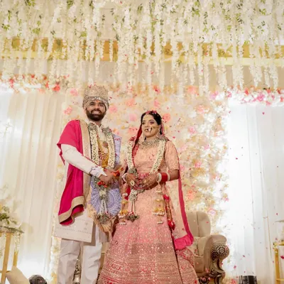 A beautiful portrait of the newly married couple during their Jaimala ceremony. They stand amidst a shower of flower petals under a stunning floral mandap, marking the beginning of their journey together.