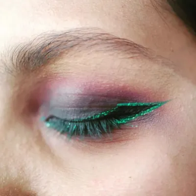 A close-up of a creative party eye makeup look. This features a purple smokey eye with a sharp, glittery green winged eyeliner, perfect for a bold and dramatic statement.