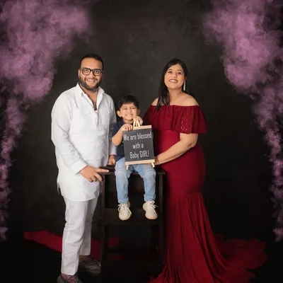 A dramatic gender reveal with vibrant pink smoke. The family stands together as the big brother-to-be holds a sign announcing they are blessed with a baby girl.