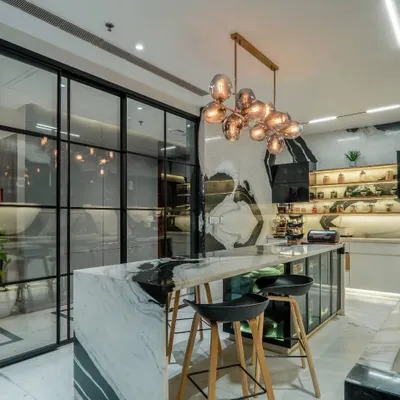 This view showcases the seamless integration of the kitchen with the adjacent space, separated by a modern, black-framed glass partition. The design ensures the kitchen feels open and connected while containing cooking activities.