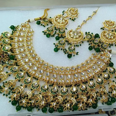 A full view of a magnificent green and gold bridal set. This rental jewellery set includes a wide choker, matching jhumkas, and a maang tikka, all featuring classic half-moon kundan work.