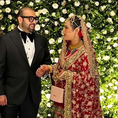 A beautiful moment between the bride and groom at their Walima reception. They are pictured against a stunning wall of white flowers, a signature of our elegant Muslim wedding decor.