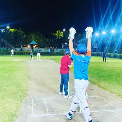 A batsman celebrates hitting the winning runs during a night match. The energy under the lights is electric, making every moment memorable.
