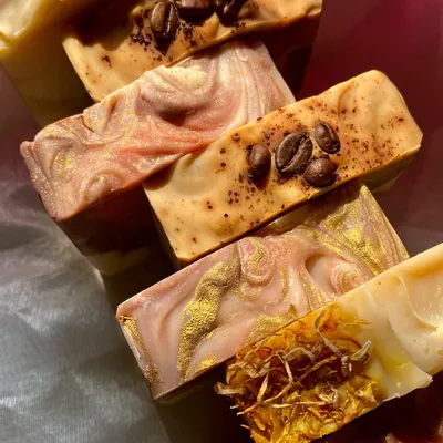A beautiful stack showcasing the variety of our artisan soaps. You can see bars topped with coffee beans and dried calendula, and others with intricate swirls of natural clays and micas.