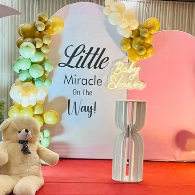 A sweet and simple baby shower setup with the theme "Little Miracle On The Way". The decor features pastel balloon clusters, a large teddy bear, and a neon sign.