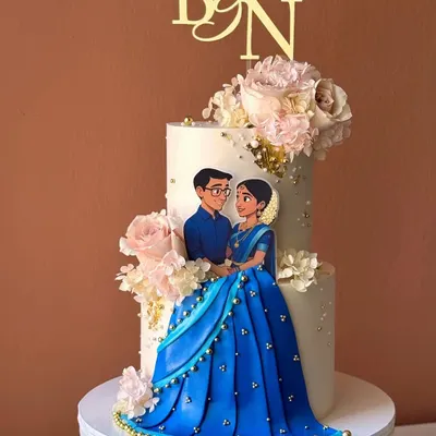 A beautiful two-tiered engagement cake celebrating an Indian couple. This design features a custom illustrated topper and is adorned with delicate pink roses and gold leaf.