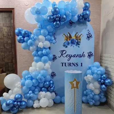 A royal blue and white theme for a first birthday. This setup includes a custom backdrop for "Reyansh Turns 1", a beautiful balloon arch, and a matching pedestal for the cake.