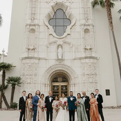 A grand family portrait outside the church, showcasing the complete, coordinated look for the Catholic wedding. From the bride's white gown and groom's teal tux to the family's attire in sage, rose gold, and navy, this is the culmination of our detailed wardrobe planning.