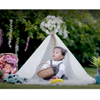 A beautifully composed outdoor kids' photoshoot featuring a toddler in a lace teepee with a basket and vintage toy car. This is an example of our fully styled portrait sessions.