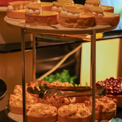 A two-tiered stand showcasing an array of our dessert offerings, including delicate lemon meringue tarts and rustic apple crumbles. There is a sweet for every tooth.