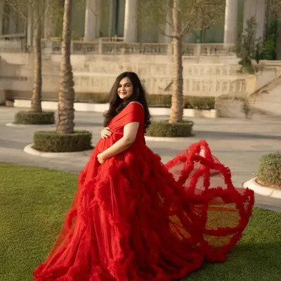 This dramatic shot showcases the incredible train of the red gown against a manicured green lawn and grand architecture. It’s a perfect blend of natural beauty and high-fashion elegance for an outdoor maternity shoot.
