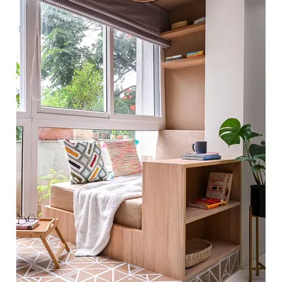 This enclosed balcony was transformed into a tranquil escape. It features a study nook on one side and a cozy low-seating area with bookshelves on the other, all defined by a warm terracotta color that matches the floor tiles.