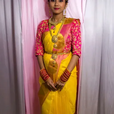 This is a classic yellow silk saree paired with a vibrant pink embroidered blouse. It's a complete traditional look, including jewelry, available for rent for pujas or ceremonies.