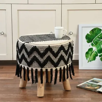 This black and white zig-zag patterned boho stool with fringes is a modern take on bohemian design. It's a versatile piece that works as a seat, footrest, or accent table.