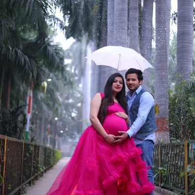 A romantic outdoor couple's portrait in a park setting. The mother-to-be's vibrant pink gown stands out beautifully against the greenery.