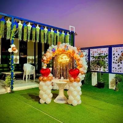 A gorgeous terrace birthday party setup at dusk. The circular balloon arch in white and bronze, accented with heart-shaped balloons, creates a stunning backdrop against the evening sky.