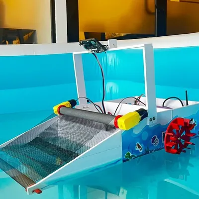 A close-up of the AI-powered river cleaning robot, showing the conveyor belt collection system, paddle wheel for propulsion, and the mounted AI camera that serves as the robot's "eyes."