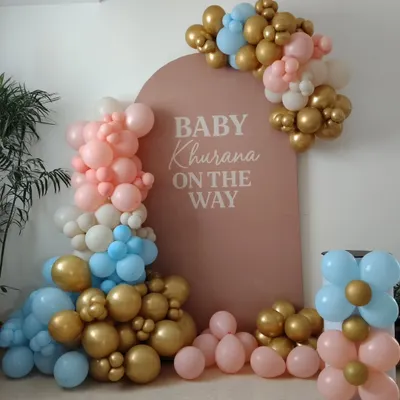 This is a popular setup for a gender reveal party, featuring a 'Baby on the Way' backdrop personalized with the family name. The balloon arrangement uses a mix of pink, blue, and metallic gold to build anticipation for the big announcement.