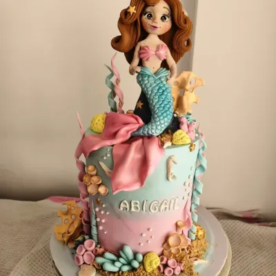 This mermaid cake for Abigail’s first birthday was an underwater dream. The centerpiece is a hand-sculpted mermaid with flowing hair, surrounded by edible coral, seashells, and starfish. The pink and teal ombre effect creates a beautiful ocean backdrop for a magical celebration.
