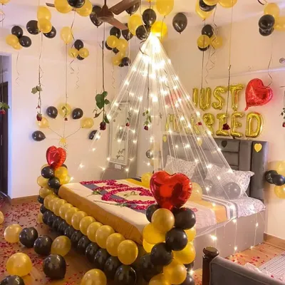 A "Just Married" first-night room decoration featuring a fairy light canopy over the bed, black and gold balloons, and scattered rose petals.