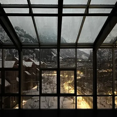 A view from within the Hamsa Resort in Manali on a winter evening. The steel-framed glass enclosure provides an uninterrupted connection to the snow-covered landscape, blending the boundary between the interior and the Himalayan outdoors.