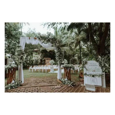 A graceful entrance for a white wedding, featuring a draped arch adorned with baby's breath and greenery. A personalized welcome sign and floral arrangements on wooden stands complete the elegant look.