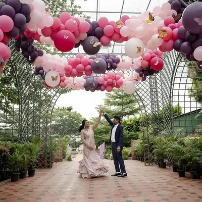 A couple dances under a spectacular balloon archway at a celebration. The vibrant pink and purple balloons create a fun and festive pathway, perfect for a milestone birthday or anniversary party.