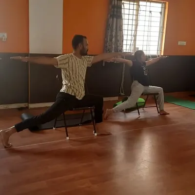 A class practices a supported Virabhadrasana (Warrior Pose) using chairs. This modification helps build strength and stability without putting pressure on the knees, making it ideal for a diverse group of employees.