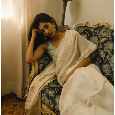 A moody and elegant portrait of a model in a beautiful white saree. The setting and lighting create a feeling of quiet contemplation.