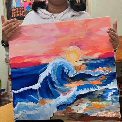 A young artist proudly presents her dynamic acrylic painting of a wave at sunset. Our classes encourage bold colors and expressive brushwork.