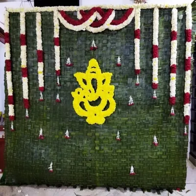 I create unique, natural backdrops for poojas, such as this wall made of fresh banana leaves featuring a Ganesha motif crafted from yellow flowers.