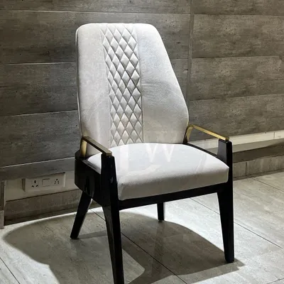 This dining chair is a perfect example of mixed-material design. It features a high back with quilted detailing, a solid wood frame, and elegant metal armrests for a truly luxurious feel.
