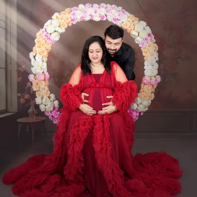 A classic pose with a modern twist. The mom-to-be is seated in a floral hoop, wearing a dramatic red gown, creating a portrait that is both romantic and powerful.