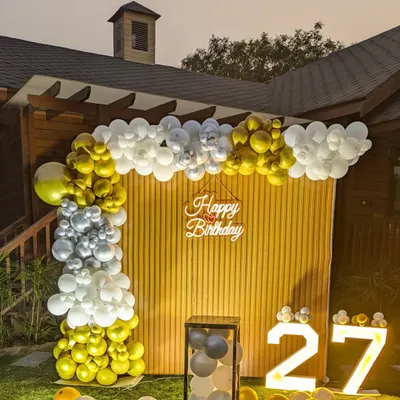 A daytime view of the 27th birthday garden party setup, showing the gold, silver, and white balloon arch against the wooden backdrop.