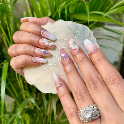 Step into a garden of elegance with these 3D floral and stone nails. This bridal set features a soft ombré base, hand-sculpted white flowers, and carefully placed iridescent stones.