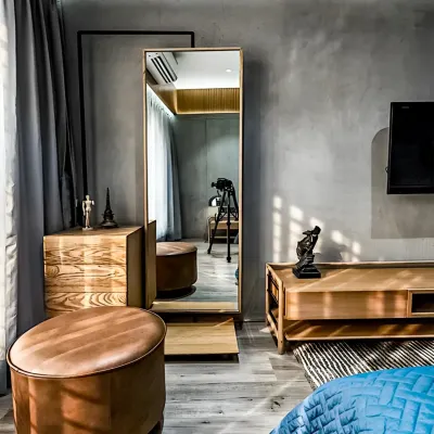 This bedroom corner is designed for getting ready in style, with a full-length mirror, a wooden dresser, and comfortable leather ottomans. The concrete-finish wall adds an industrial-chic touch to the warm and inviting space.